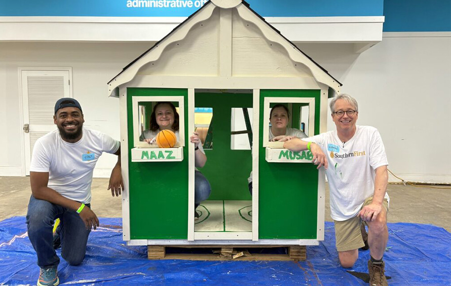 Four Greensboro bankers volunteering, posing with a children's playhouse they constructed.